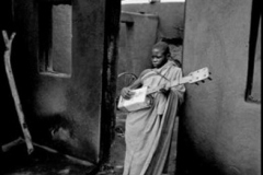LESOTHO. Maseru. Boy playing oil can guitar in the burned out ruins of his home during racial riot. 1961.