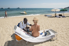 Title: Saint Tropez, France
A Senegalese migrant sells a bracelet to a naked lady on a naturist strech of Pampelonne Beach in Saint Tropez.
From the series 'The Continuity of Man', a portrait of the Mediterranean region.
©Nick Hannes
